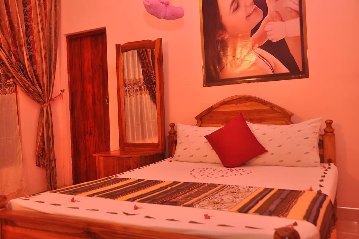 A bedroom with a wooden bed, a red pillow, and a heart-shaped decoration on the bedspread.