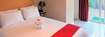 Una cama bien hecha con sábanas blancas y una manta roja, una lámpara y vistas al exterior a través de una puerta corredera.