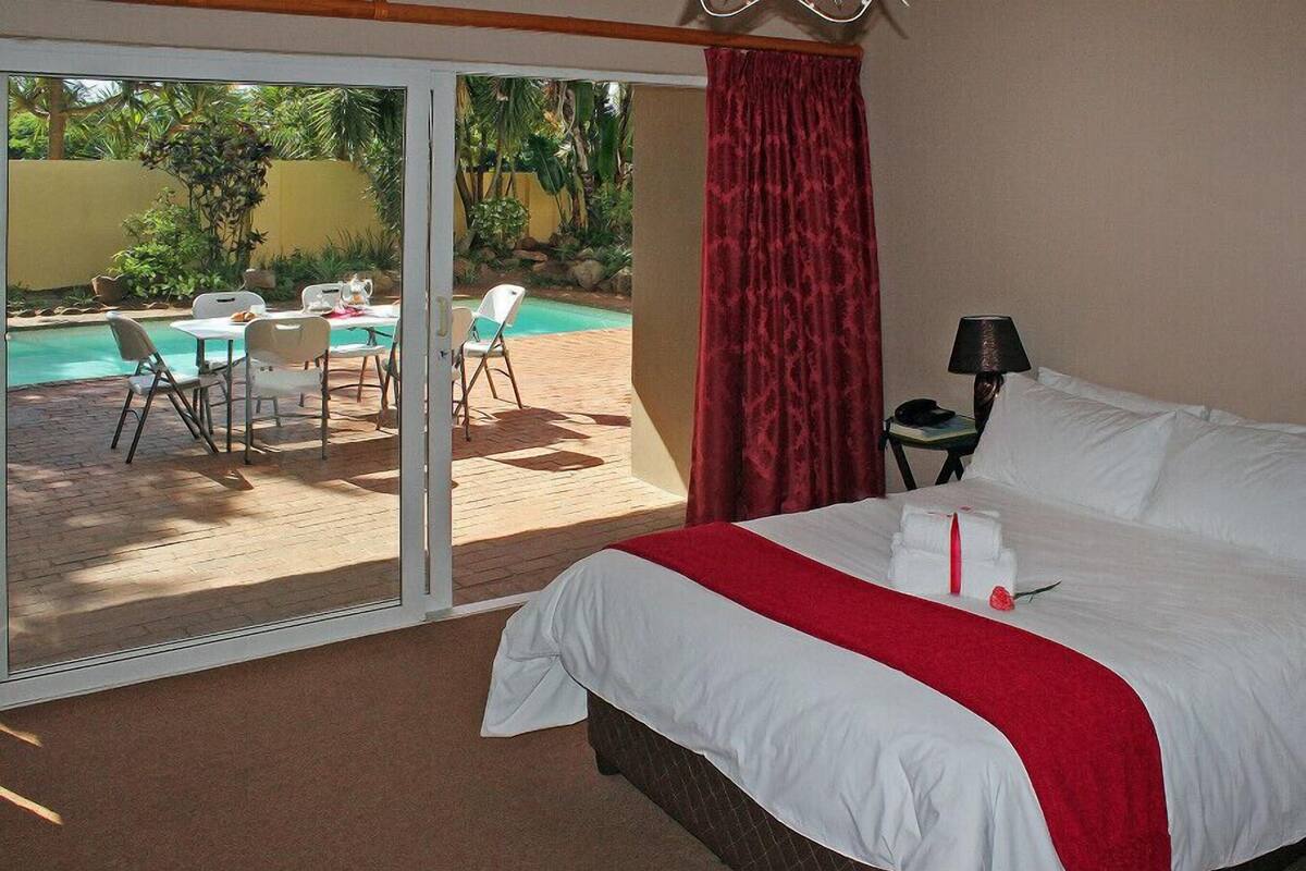 Quarto de hotel com cama, escrivaninha, cadeira, luminária e vista para uma piscina e área de estar ao ar livre.
