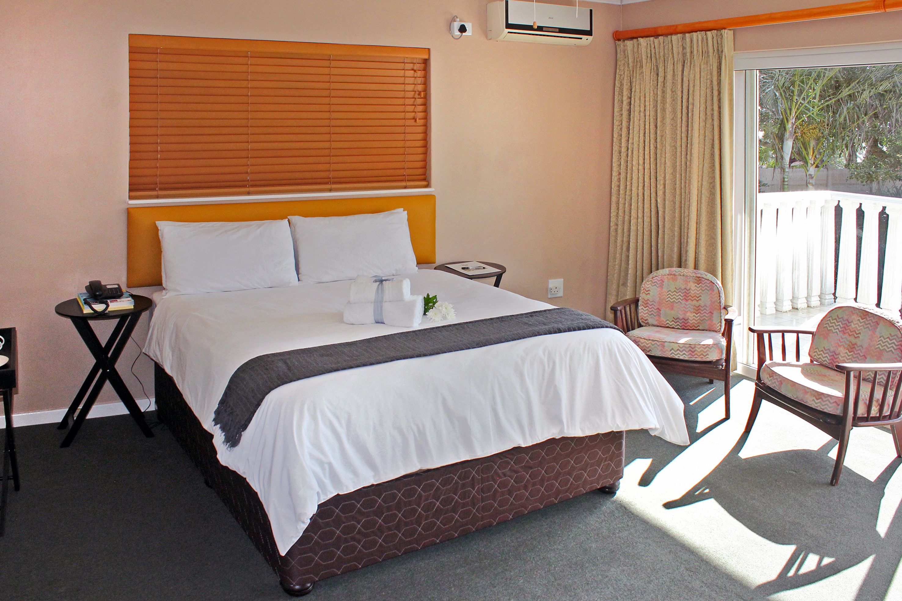 A hotel room with a bed, a small table, a chair, and a balcony with a view.