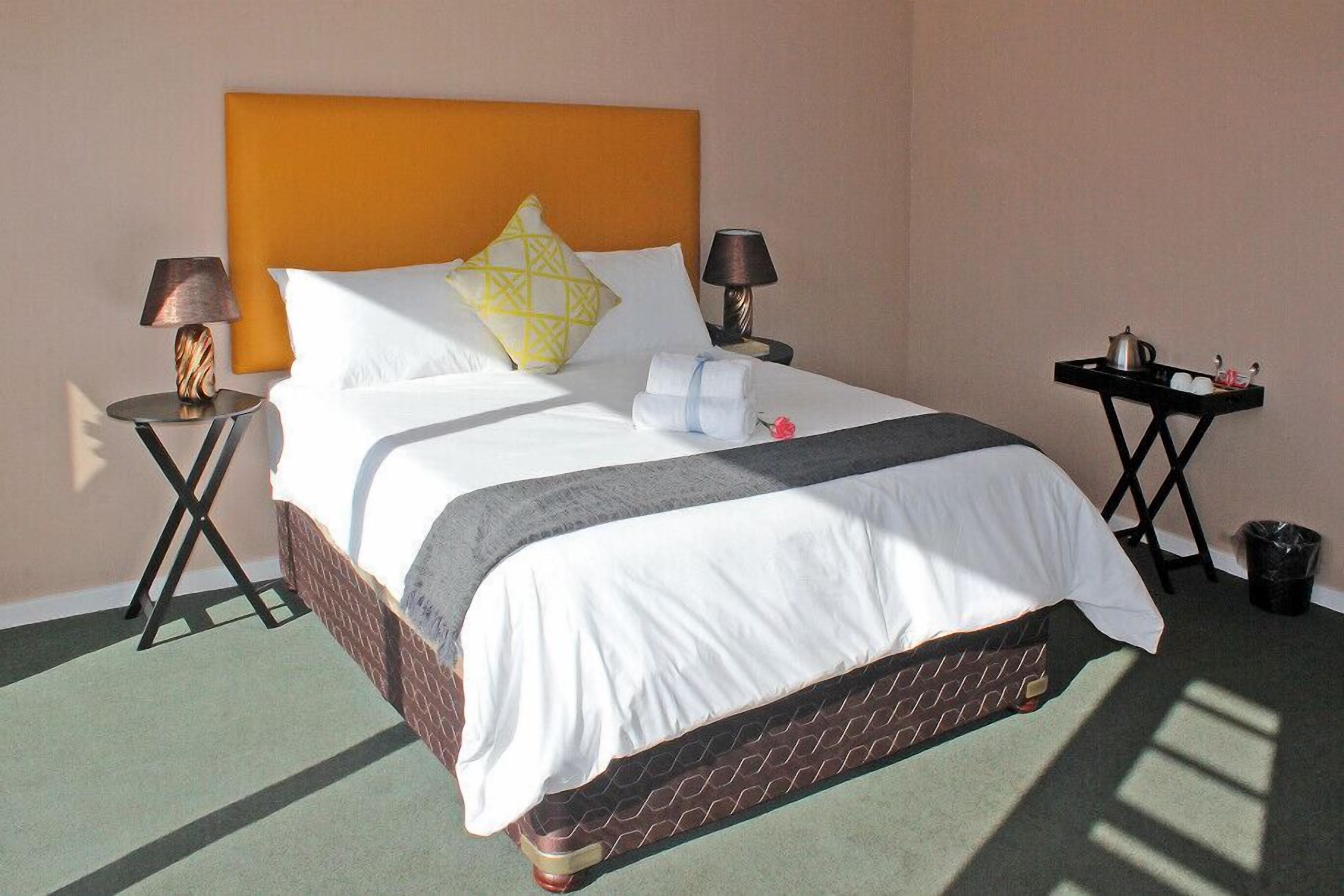A hotel room with a large bed, two bedside tables, a nightstand, a tray table, and a trash bin.