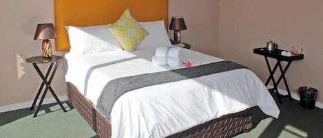 A hotel room with a large bed, two bedside tables, a nightstand, a tray table, and a trash bin.