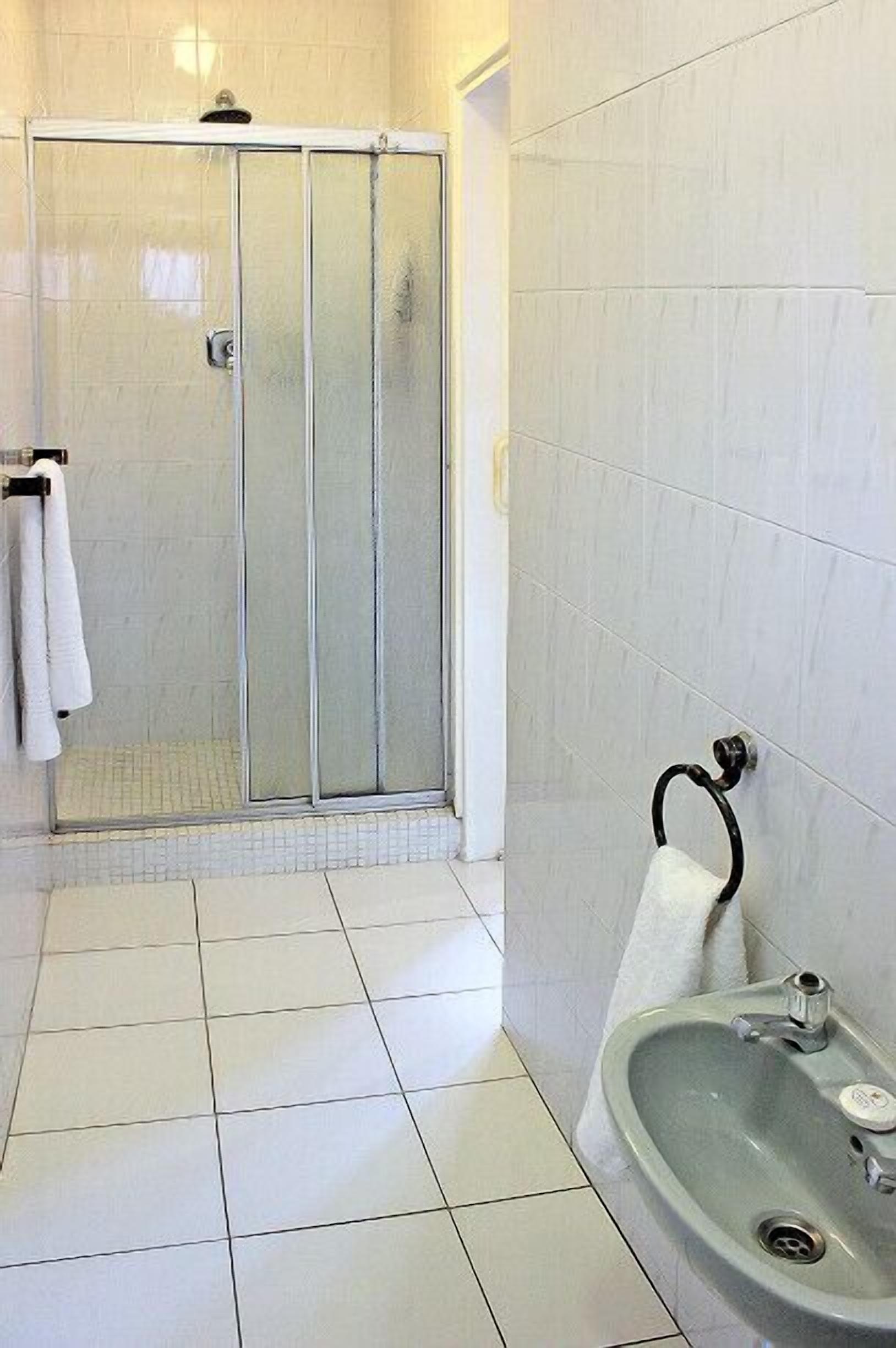 Ein Badezimmer mit Duschkabine aus Glas, Waschbecken mit Handtuchhalter und weiß gefliestem Boden.