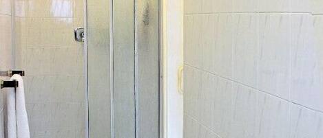 A bathroom with a glass shower enclosure, a sink with a towel ring, and white tiled flooring.