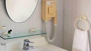 Un baño con lavamanos blanco, estante de vidrio con artículos de aseo, espejo y argolla para toallas.
