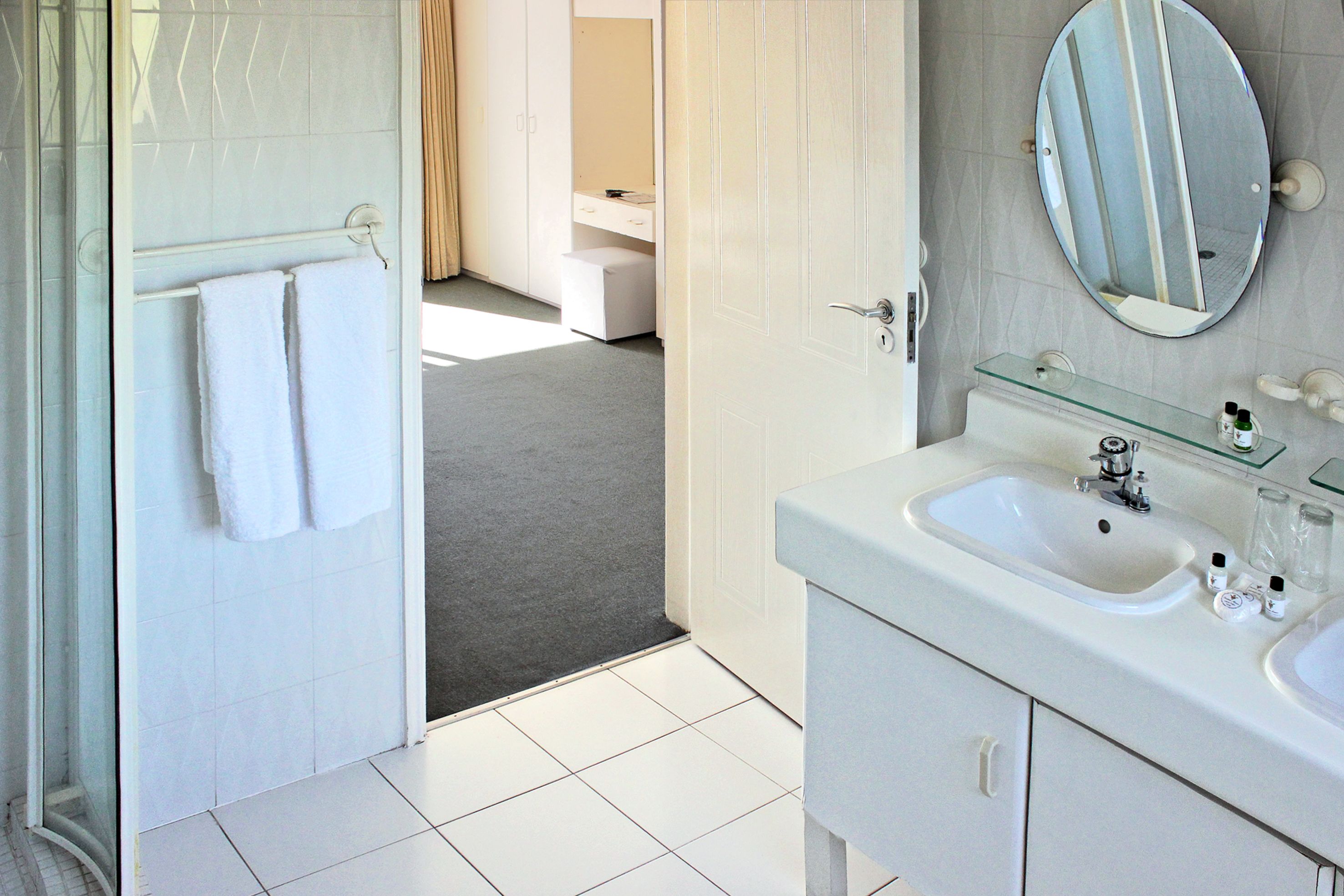 A modern bathroom with a white sink, mirror, and glass shelf.