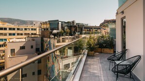 A modern urban balcony with a glass railing, potted plants, and outdoor seating.