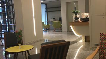 A modern lobby with a reception desk, seating area, and a staircase.