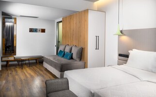 Ένα σύγχρονο υπνοδωμάτιο με έναν γκρι καναπέ, ένα κρεβάτι, μια ξύλινη ντουλάπα και ένα γραφείο με καρέκλα.