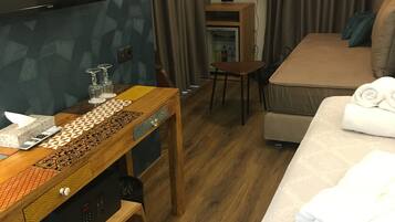 A hotel room with a bed, a wooden table with a patterned design, a television mounted on the wall, a small cabinet, and a round floor lamp.