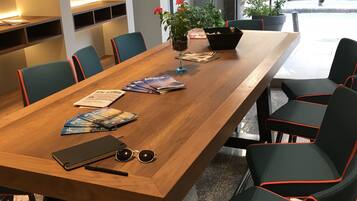 Een moderne eetruimte met een lange houten tafel, zwarte en blauwgroene stoelen en een potplant.