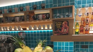 A bar area with a fruit bowl containing pineapple, melon, and lime, a Moët glass, and a cocktail shaker.