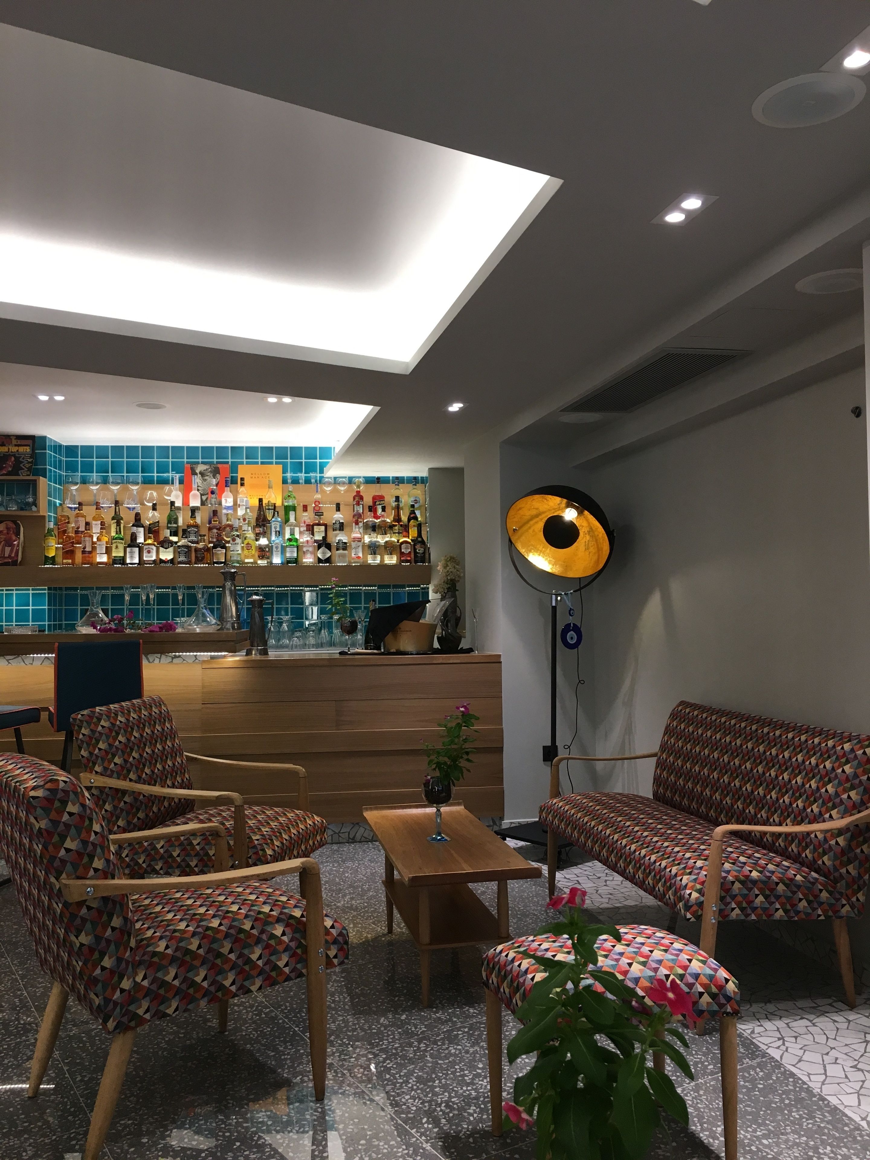 A bar area with a variety of liquor bottles, a seating area with patterned chairs and a table, and a large floor lamp.