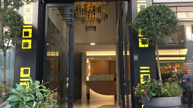 A hotel entrance with a modern design, featuring a glass door, a reception desk, and a decorative ceiling.