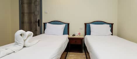 Een hotelkamer met twee bedden, een houten nachtkastje ertussen en een handdoekfiguur op het linkerbed.