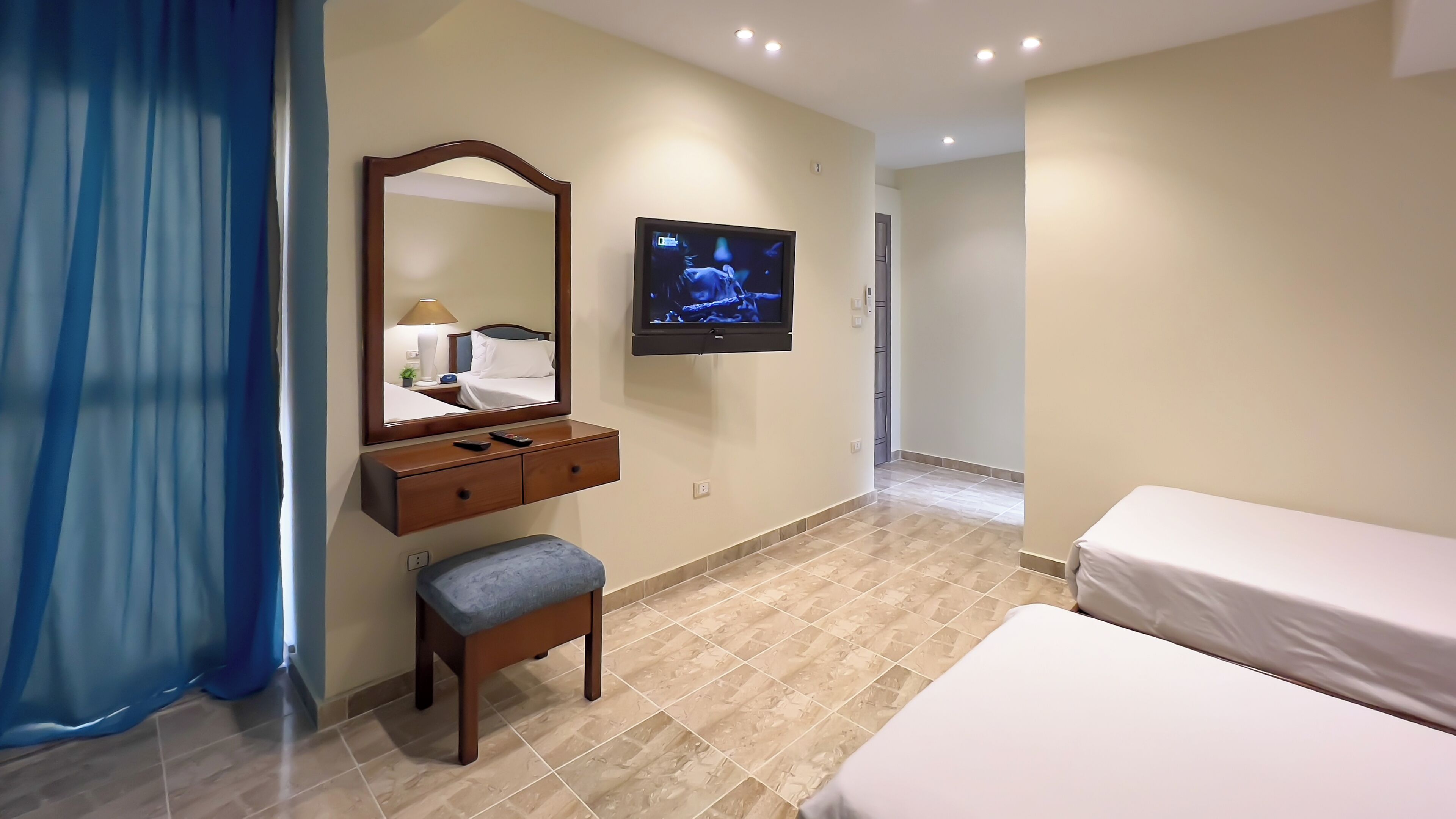 A hotel room with a bed, a TV mounted on the wall, a wooden dresser, and a bench.