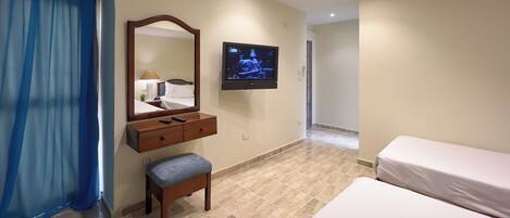 A hotel room with a bed, a TV mounted on the wall, a wooden dresser, and a bench.