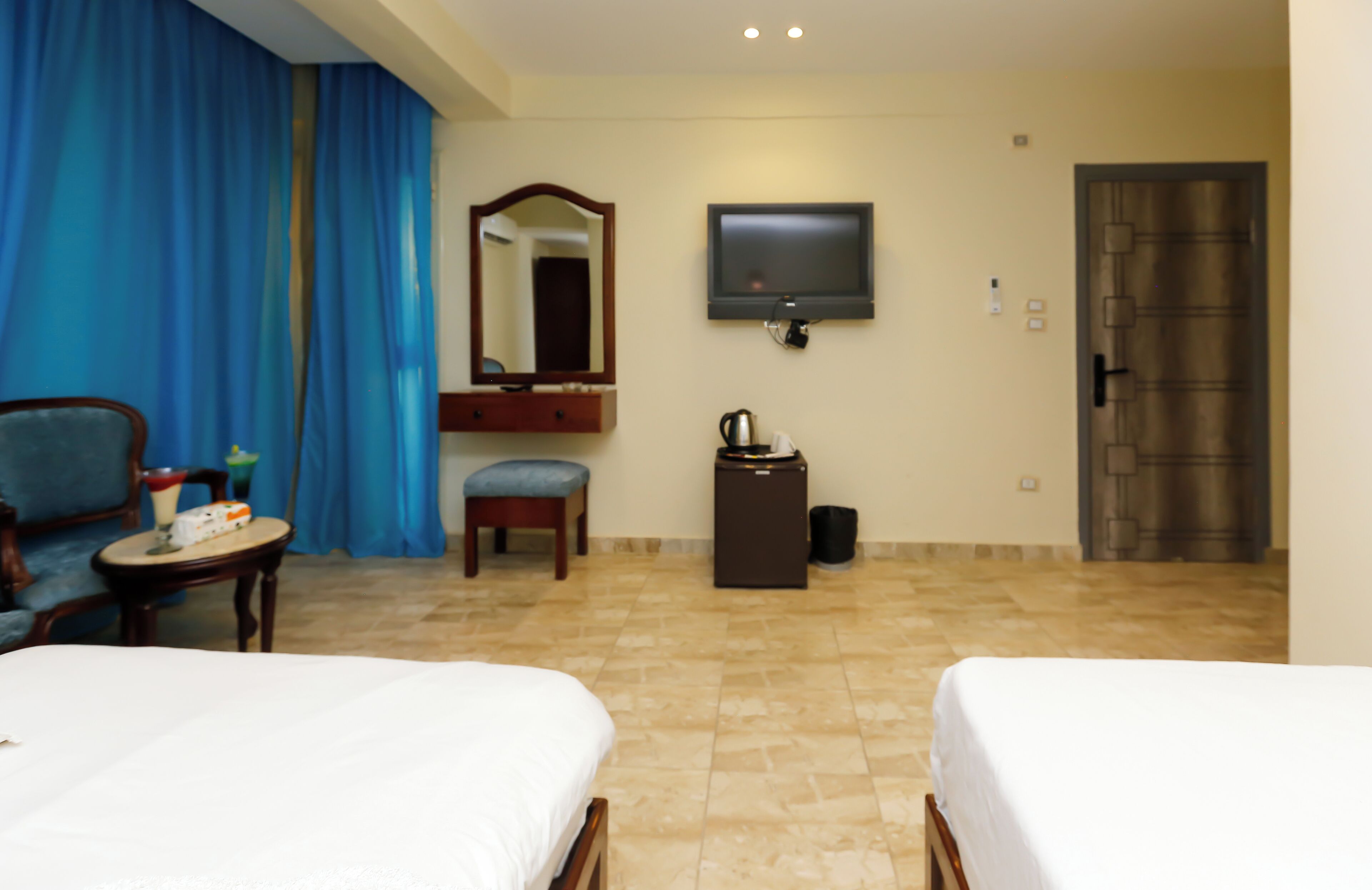 A hotel room with two beds, a television, a mirror, a small table with a kettle, and a trash bin.