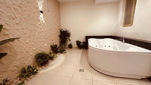 A modern bathroom with a large bathtub, a textured wall, and a small garden area with plants. - Giza Pyramids Inn (Giza)