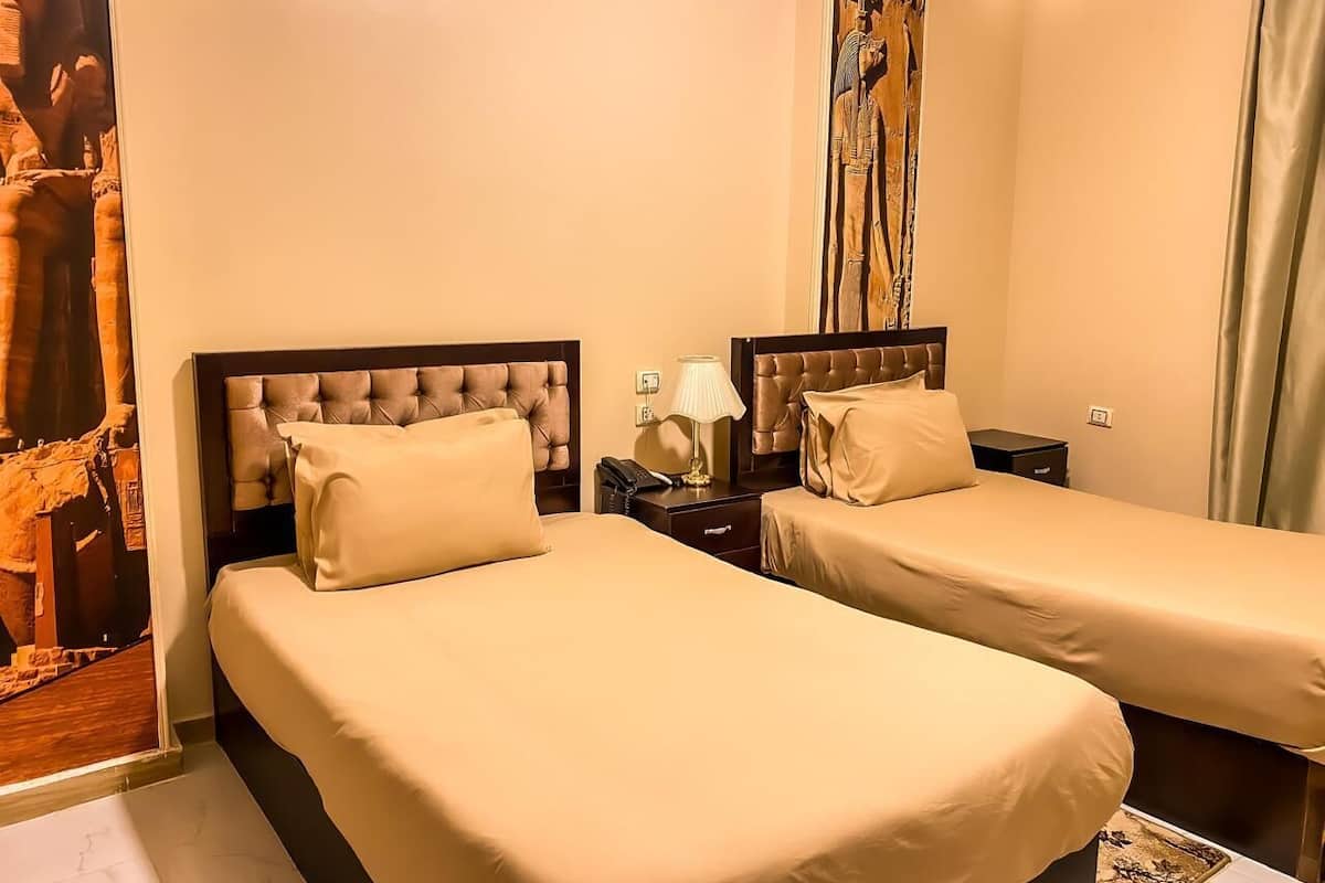 Habitación de hotel con dos camas, una mesita de noche con lámpara y un panel decorativo en la pared.