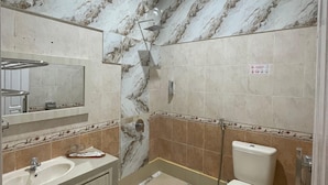 A bathroom with marble walls, a sink, a toilet, and a shower. - Soeltan Luxe Hotel (Bandar Lampung)