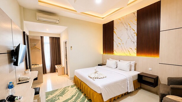 A hotel room with a bed, bedside tables, a desk, a chair, a TV, and an air conditioning unit. - Soeltan Luxe Hotel (Bandar Lampung)