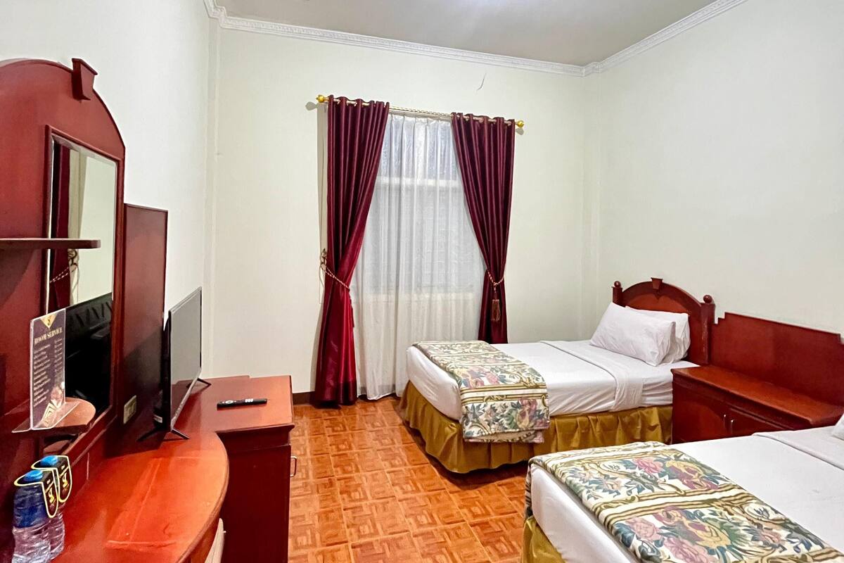 A hotel room with two single beds, a desk with a chair, a television, and a mirror.