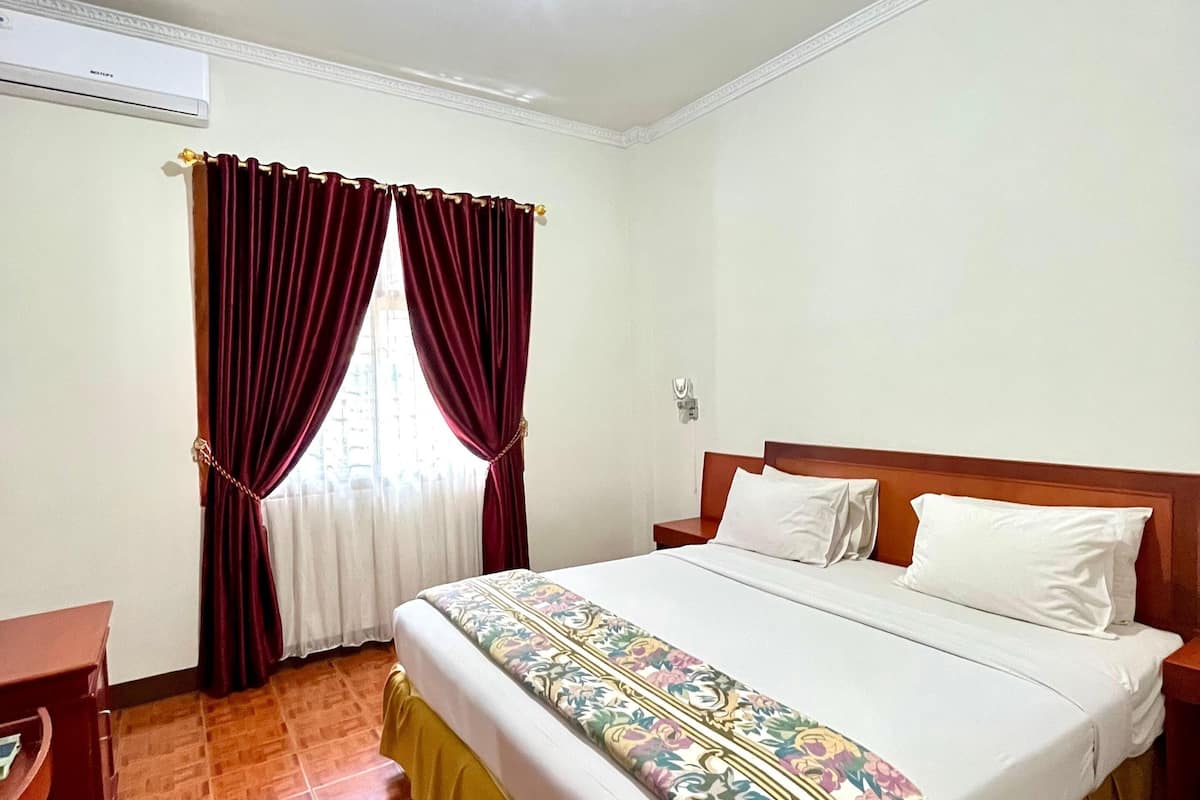 A hotel room with a bed, a nightstand, a desk, and a window with curtains.