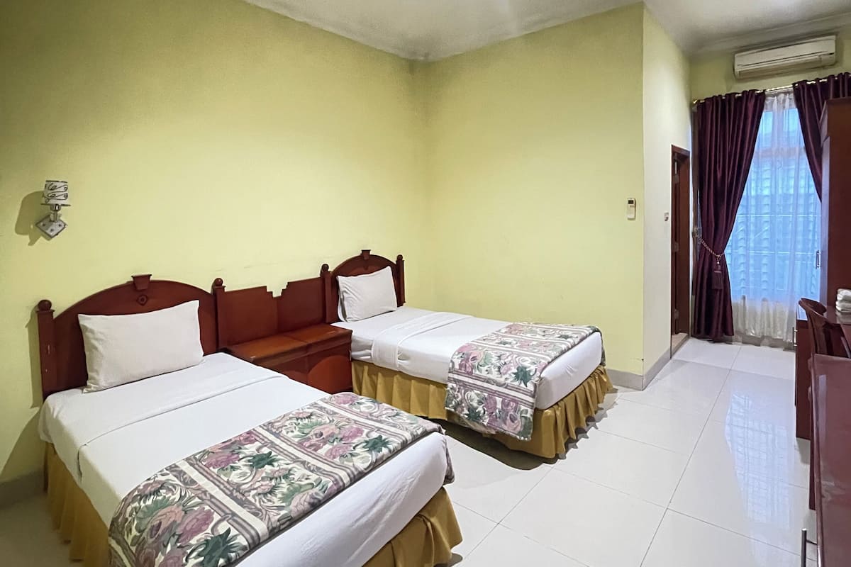 A hotel room with two beds, a wooden headboard, a nightstand, and a window with curtains.