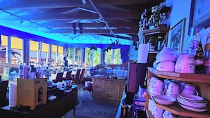 Un café acogedor, con poca luz, con muebles de madera y una variedad de tazas y platos exhibidos en estantes.