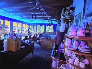 A cozy, dimly lit café with wooden furniture and a variety of mugs and plates displayed on shelves.