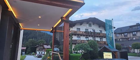 The entrance of Die Hotel Pension with a covered outdoor area and a view of the surrounding buildings and street.