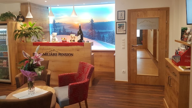 Zona de recepción con escritorio de madera, una silla roja, un jarrón de flores y un ventanal con vistas panorámicas.