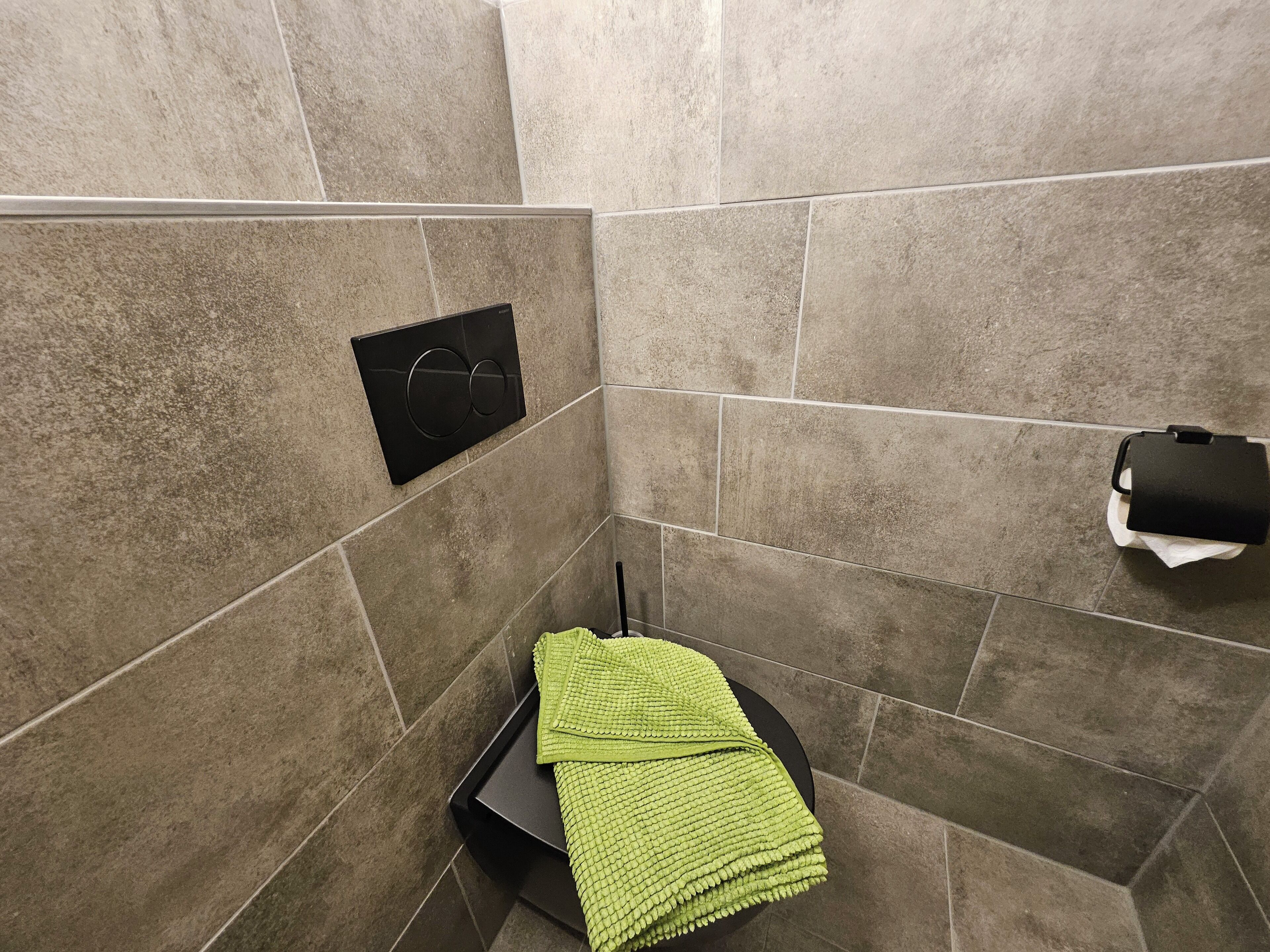 A bathroom with a towel rack, a black trash bin, and a toilet paper holder on the wall.