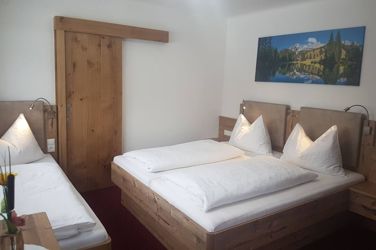 A double room with two beds, wooden headboards, a wooden door, a nightstand, a bedside table, a lamp, and a painting on the wall.