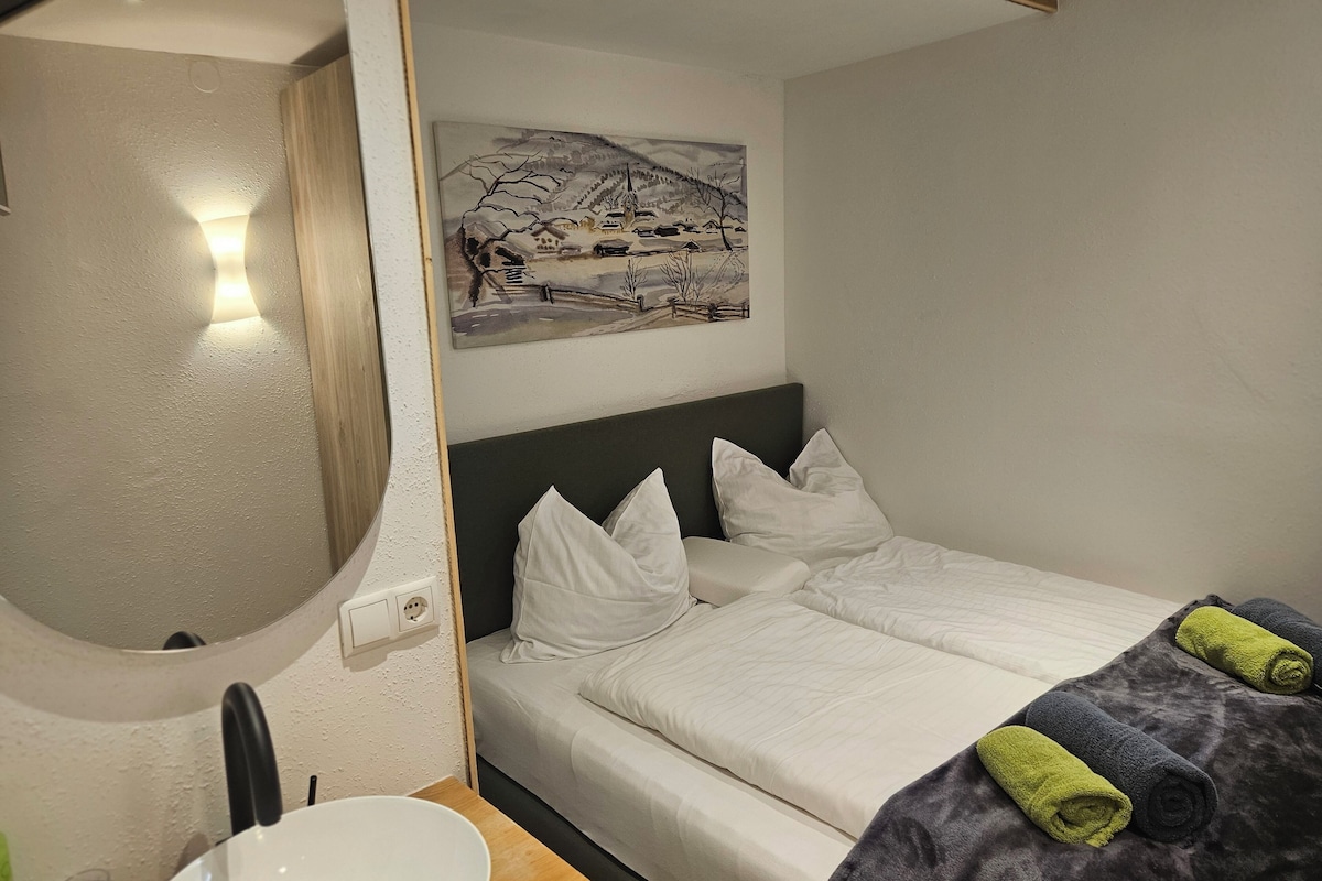 Een hotelkamer met een bed, een schilderij, een ronde spiegel en een houten tafel.