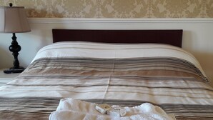 Una cama bien hecha con ropa de cama a rayas, una lámpara y una pila de toallas sobre la cama.