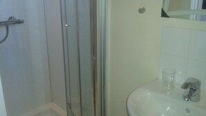 Un baño con cabina de ducha de vidrio, un lavamanos con espejo y un vaso de agua sobre el mostrador.