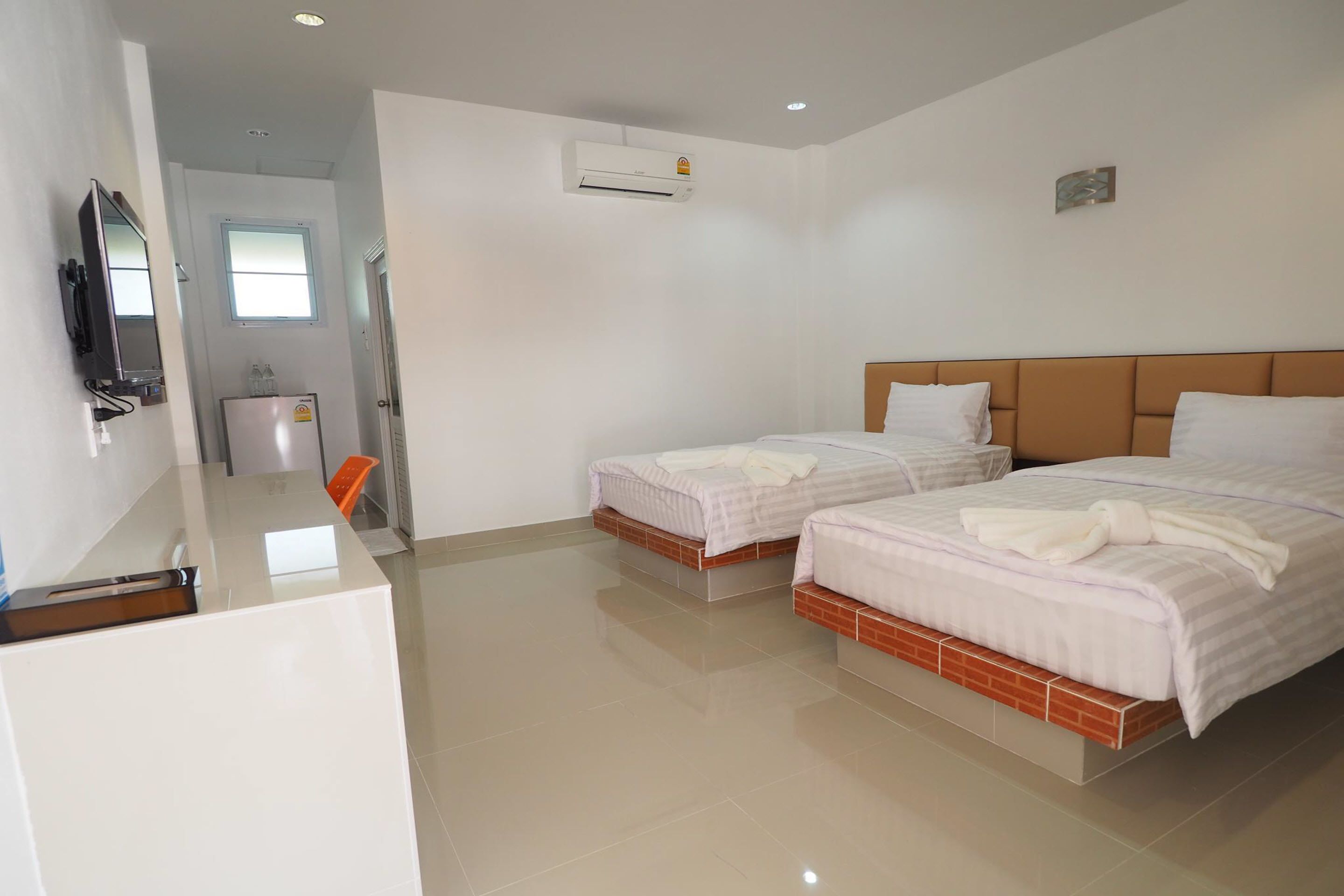 A hotel room with two beds, a TV, an air conditioner, and a window.