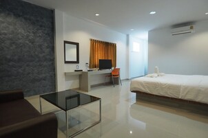 Una habitación de hotel moderna con una cama, un escritorio con computadora, una silla, una mesa de centro de vidrio y un espejo grande.