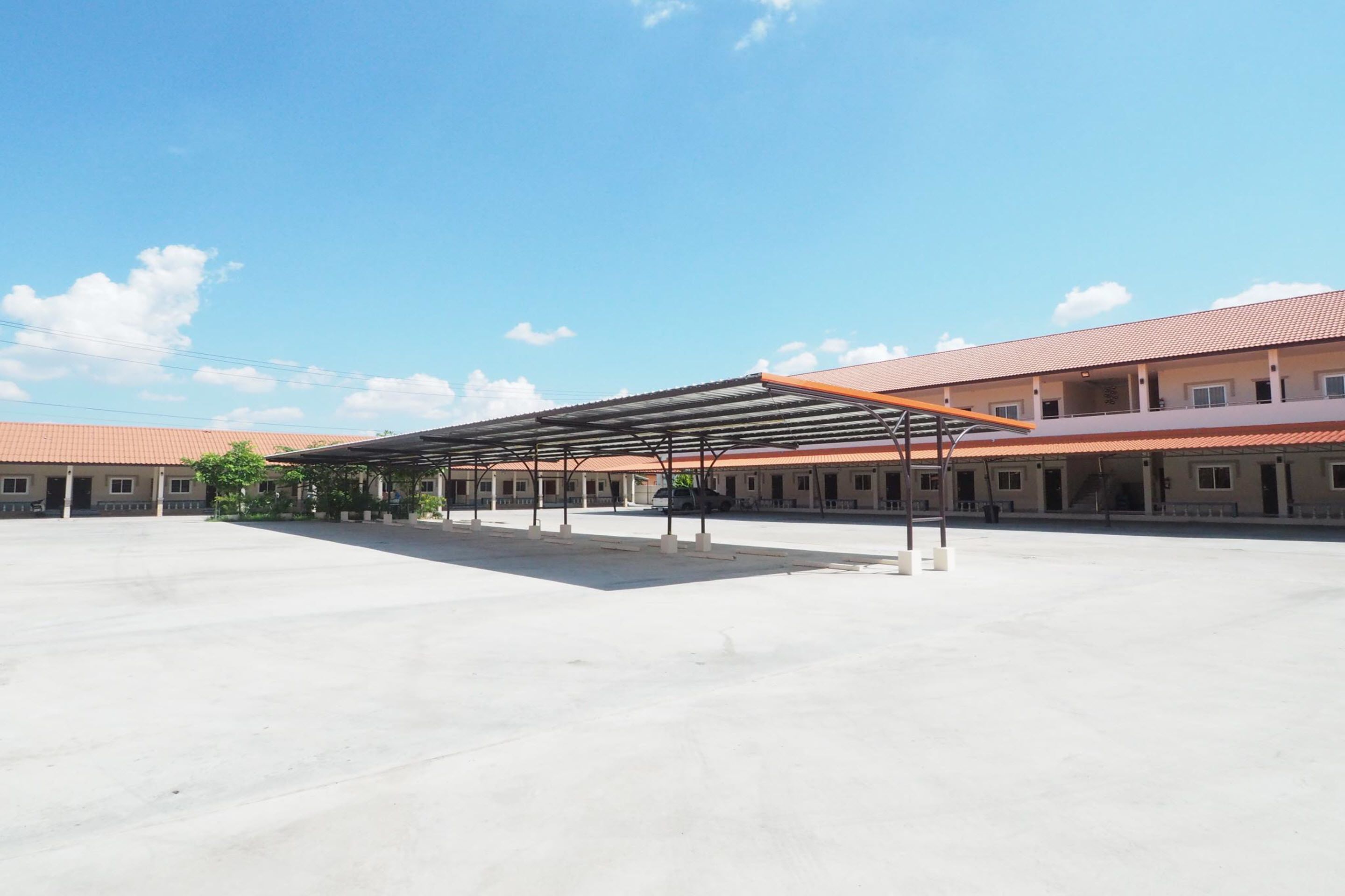 A spacious outdoor area with a covered seating area and a building with a tiled roof in the background.