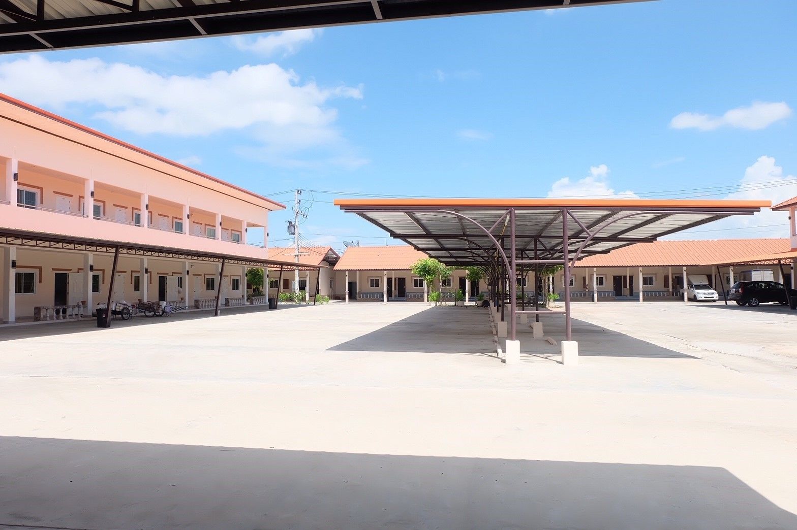 A spacious courtyard with a covered seating area, multiple buildings with red-tiled roofs, and a clear blue sky.