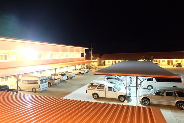 A parking area with multiple vehicles, including cars and vans, under a covered structure with a red roof.