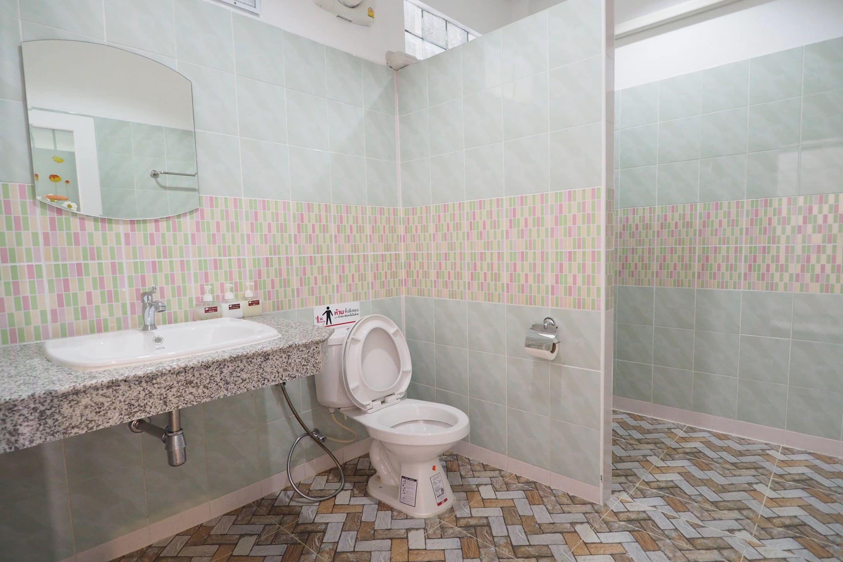 A bathroom with a sink, toilet, and mirror. The walls are tiled with a pattern, and the floor has a herringbone design.