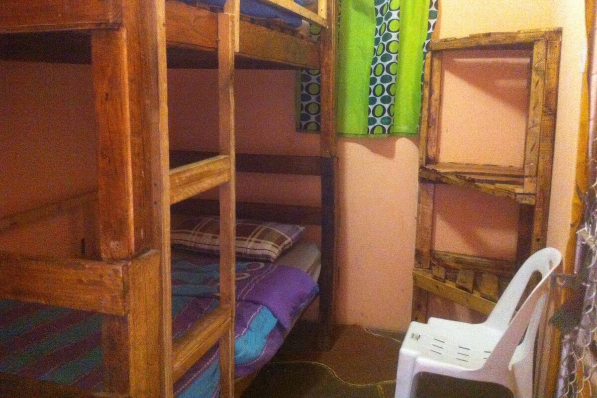 A bunk bed room with wooden bunk beds, a white plastic chair, and patterned curtains.