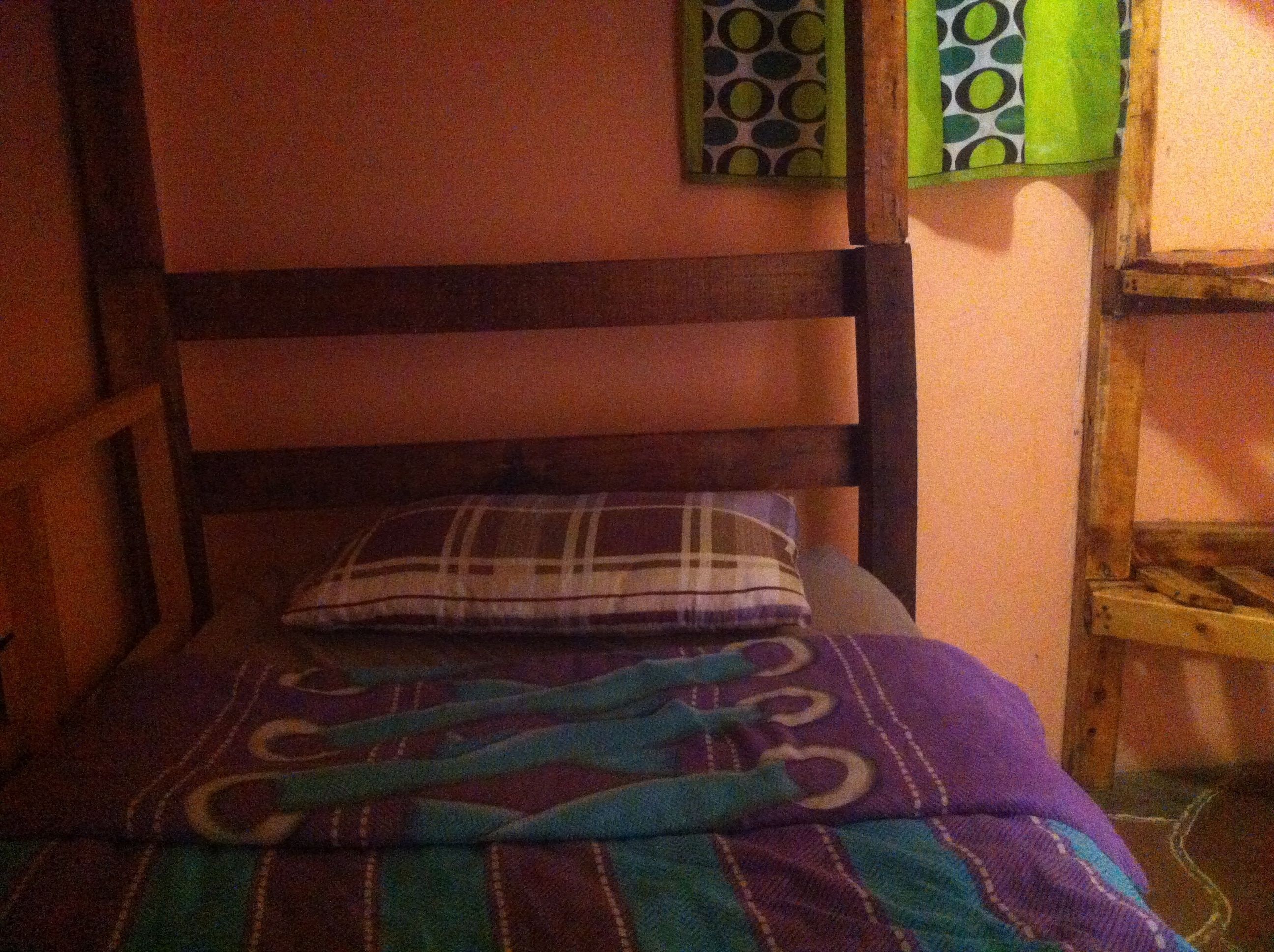 Una habitación pequeña y acogedora con una cama individual, cabecera de madera y una manta estampada.