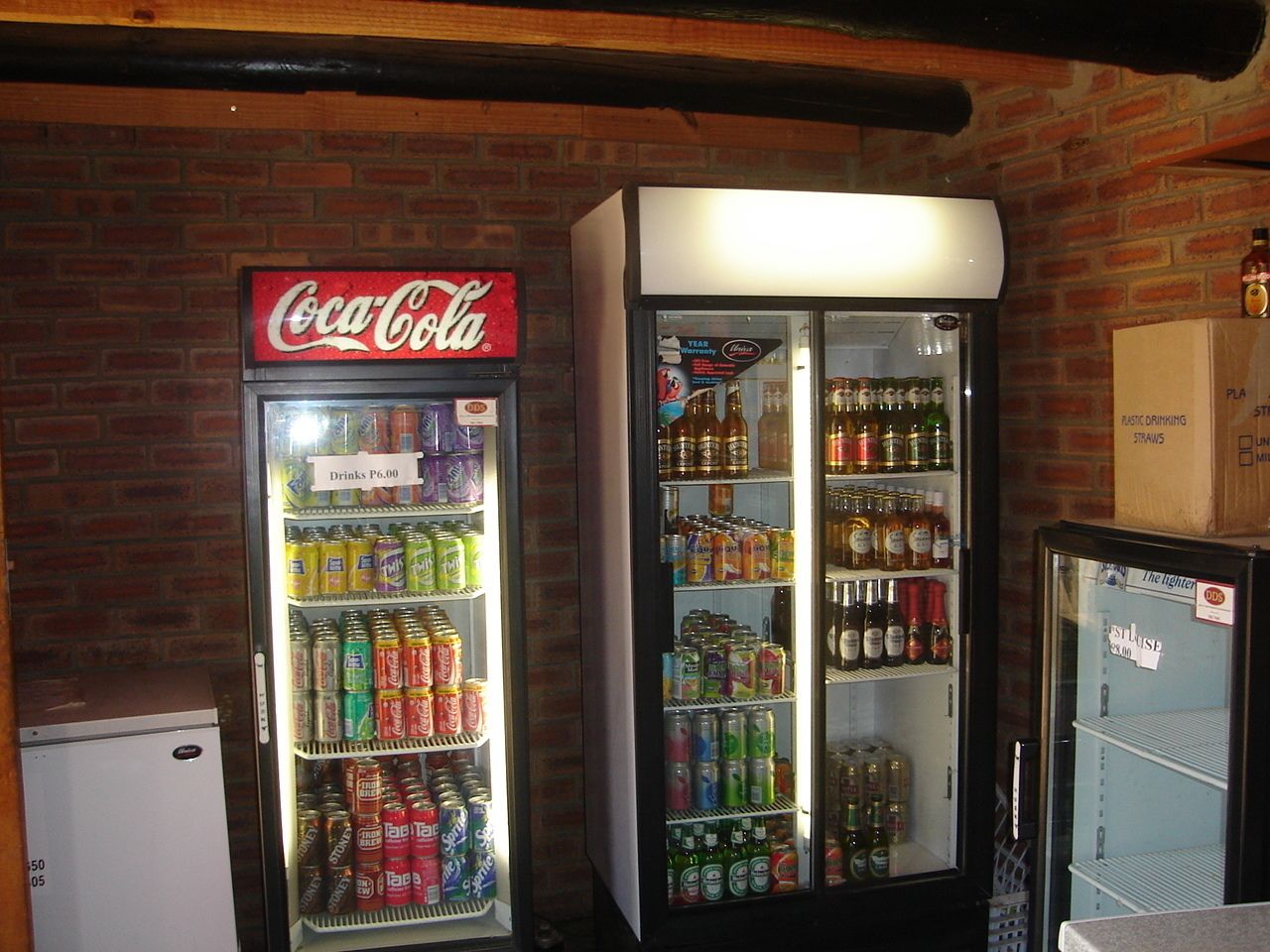 Dos máquinas expendedoras de bebidas, una marca Coca-Cola y otra con una variedad de opciones, frente a un muro de ladrillo.