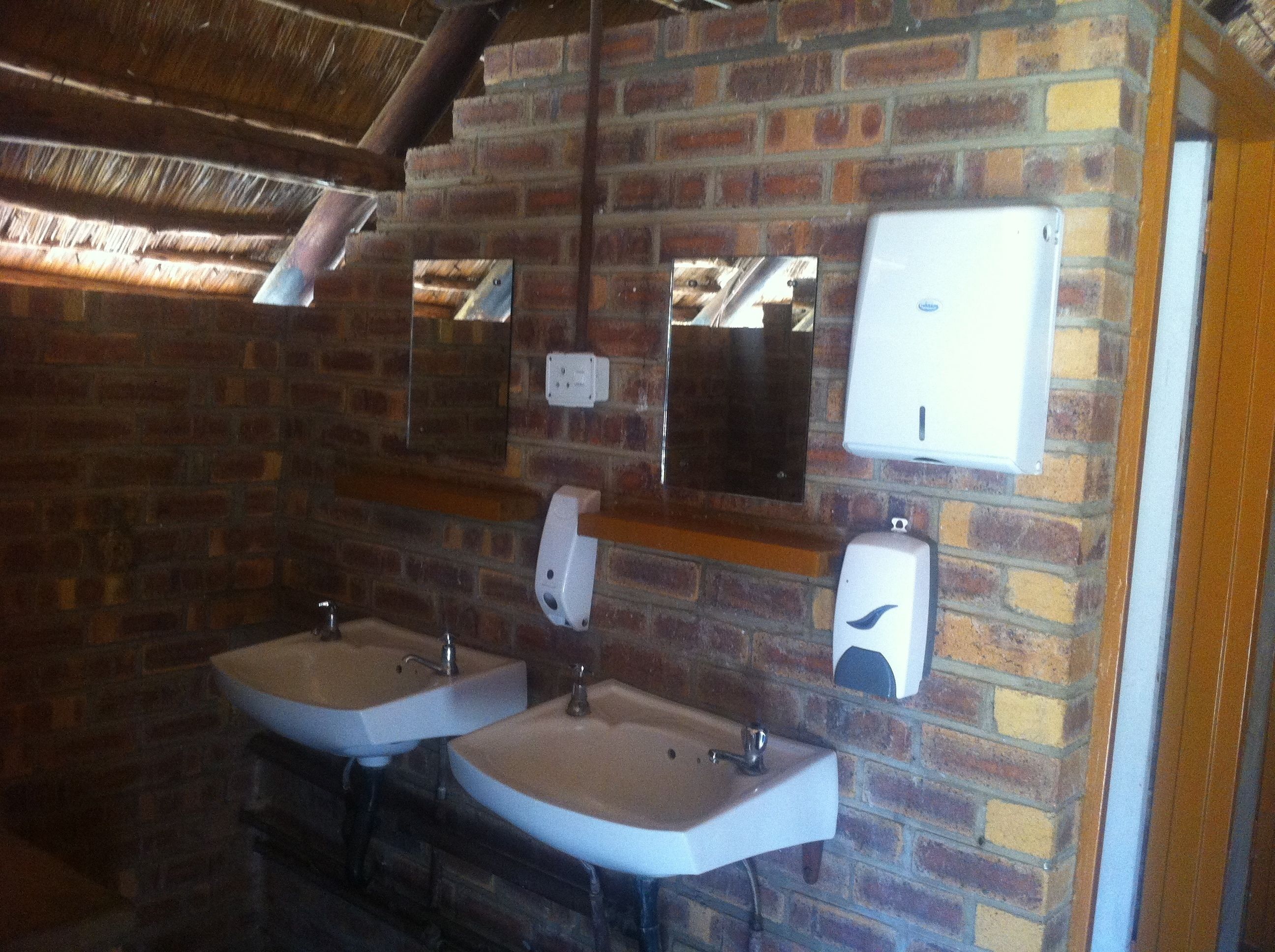A restroom with two sinks, a mirror, and a soap dispenser on the wall.