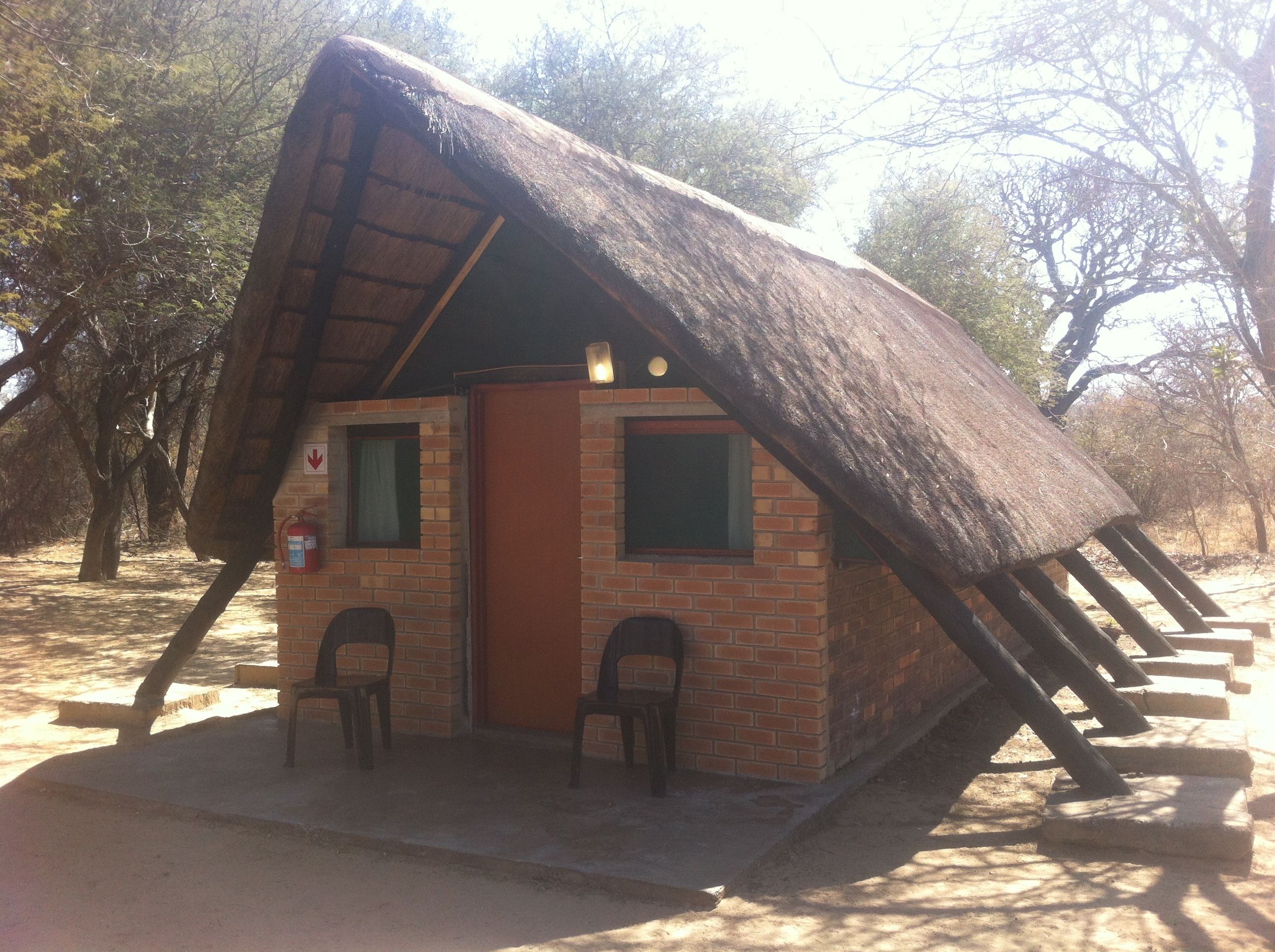 Uma cabana com telhado de palha e exterior de tijolo, duas janelas e uma porta.