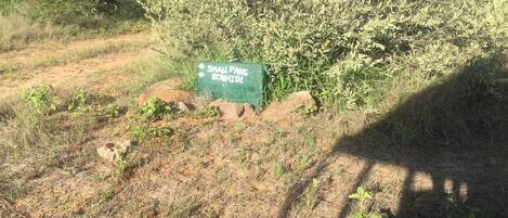 Ein Schild mit der Aufschrift 'Small Pans Bighide' in einer natürlichen Umgebung mit spärlicher Vegetation und Felsen.